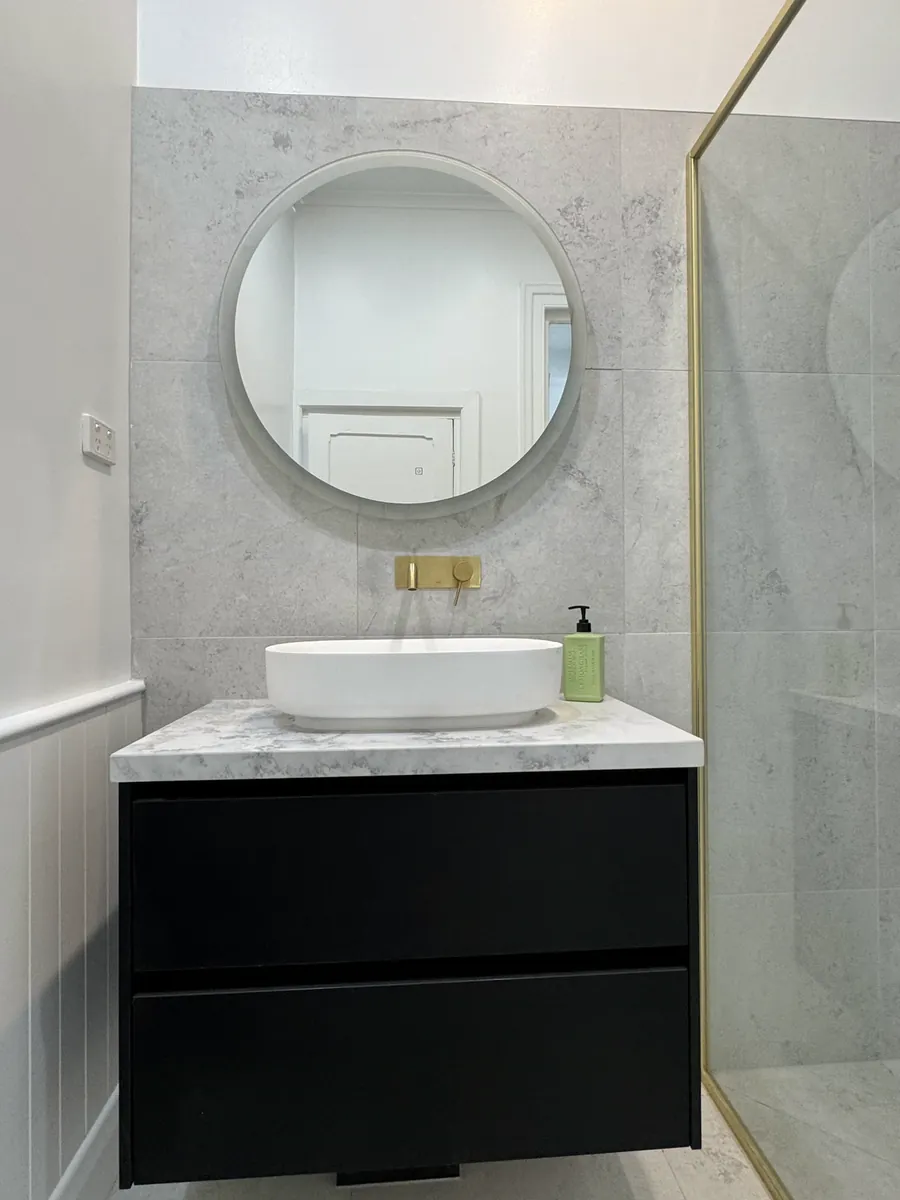 Round mirror and marble-look wall above a black vanity with a stone top