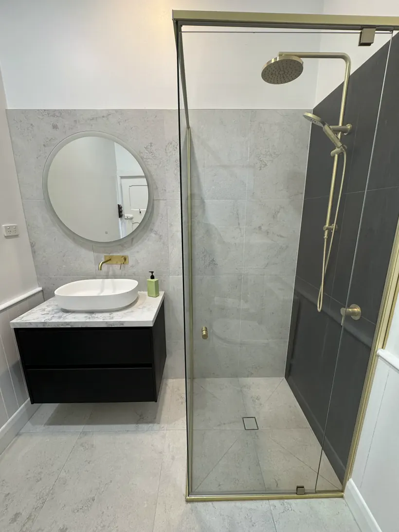 Round mirror over a black vanity with a brass framed shower screen
