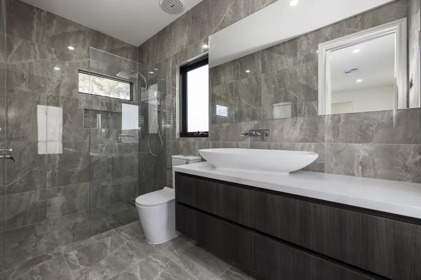 Grey stone tiled bathroom with a dark timber vanity and a full width mirror