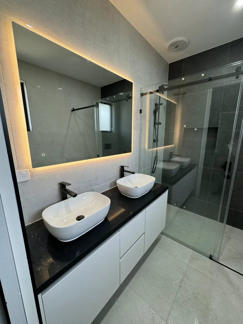 Backlit mirror above double basins set into a black benchtop