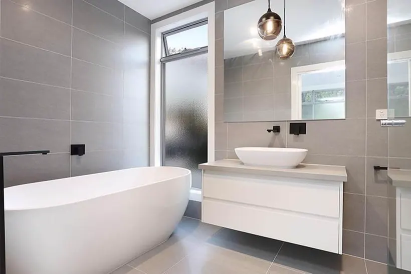 Freestanding bath under pendant lights beside a white vanity